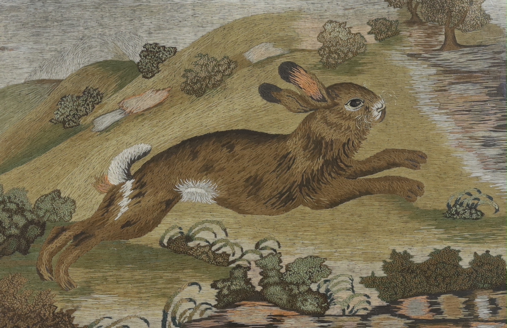 A late 19th century framed woolwork embroidered panel of a rabbit running through the countryside, worked mostly in stem stitch and raised knotting, 66.5cm wide x 42cm high